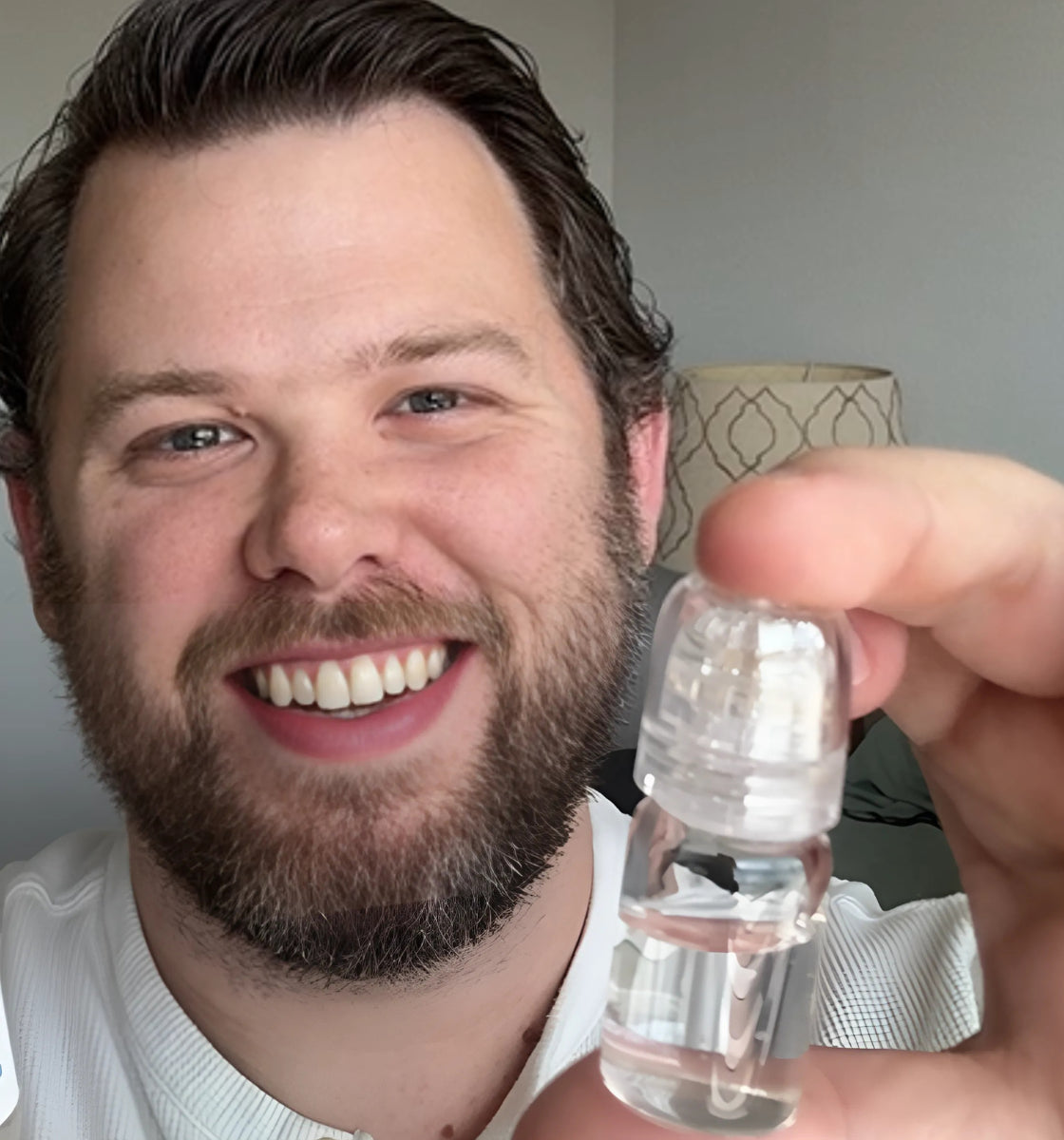 Man smiling while holding a small clear bottle.